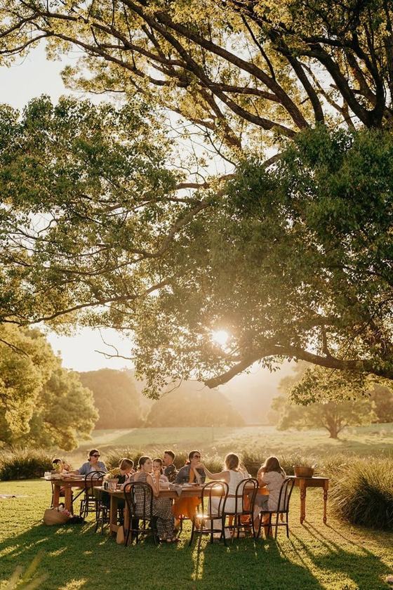 A long table beneath old trees in golden evening light