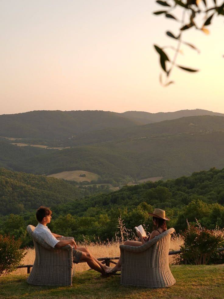 A couple sitting in garden chairs, looking out over the hills at sunset