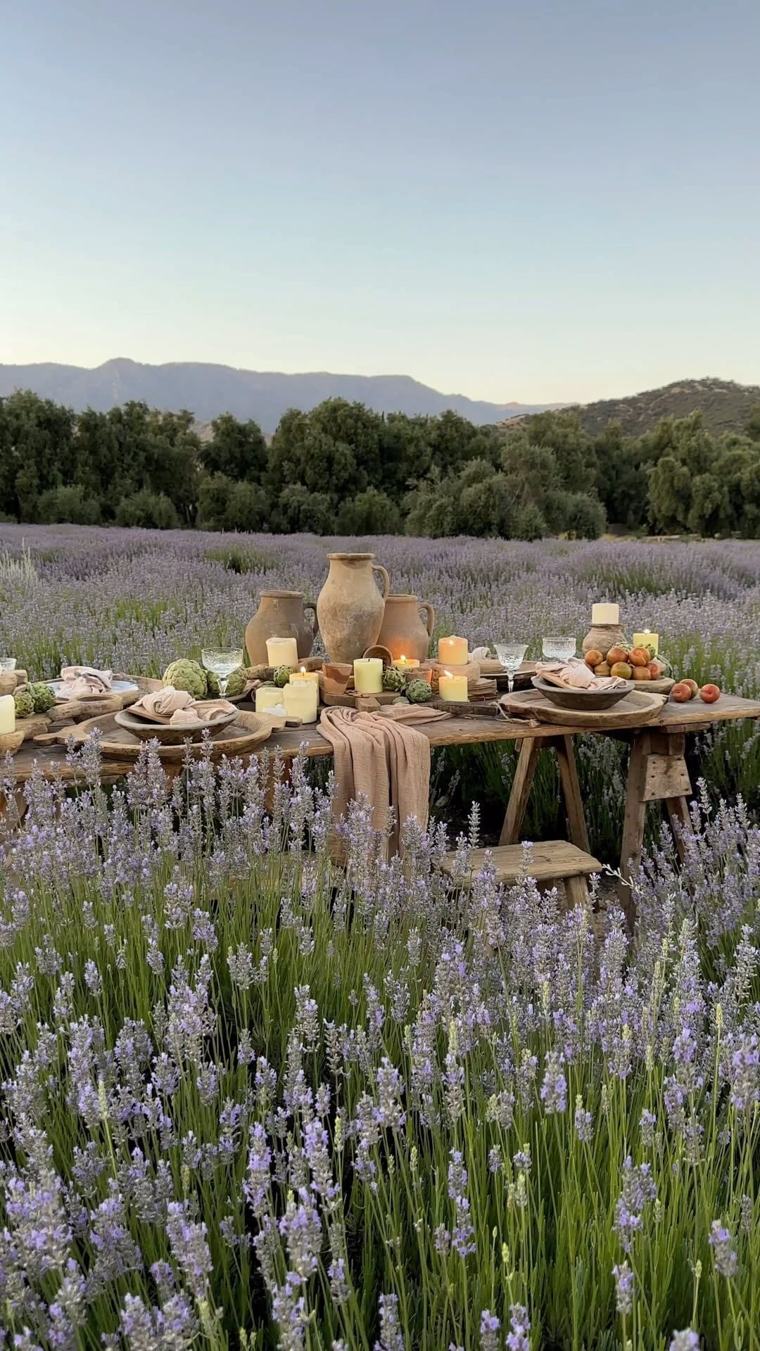 A long wooden table set with candles and earthenware in a lavender field at dusk