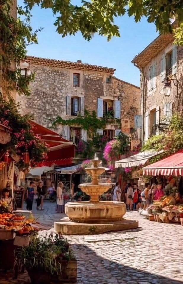 A cobbled village square in Provence with a stone fountain and striped market awnings