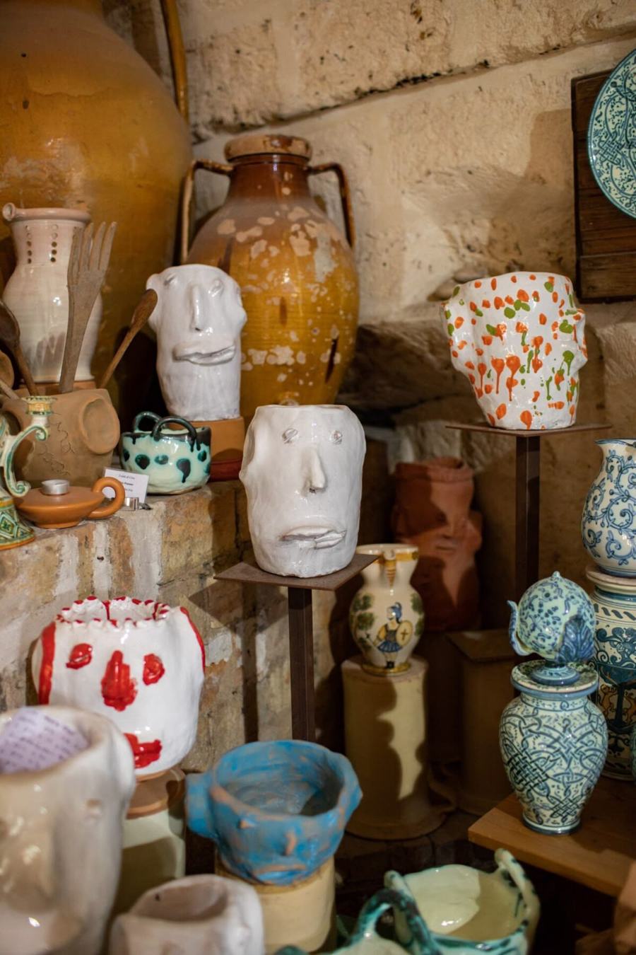 A Puglian ceramics workshop, hand-painted jugs and face vases on stone shelves beside a great olive oil jar
