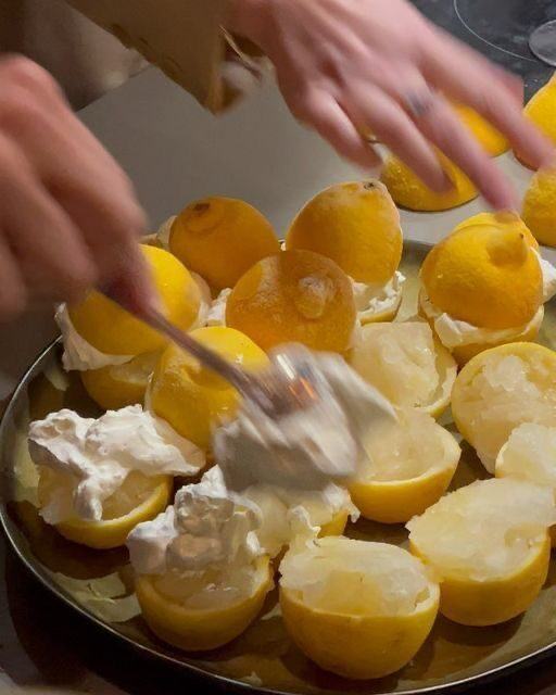 Hands filling hollowed lemons with cream at a kitchen counter
