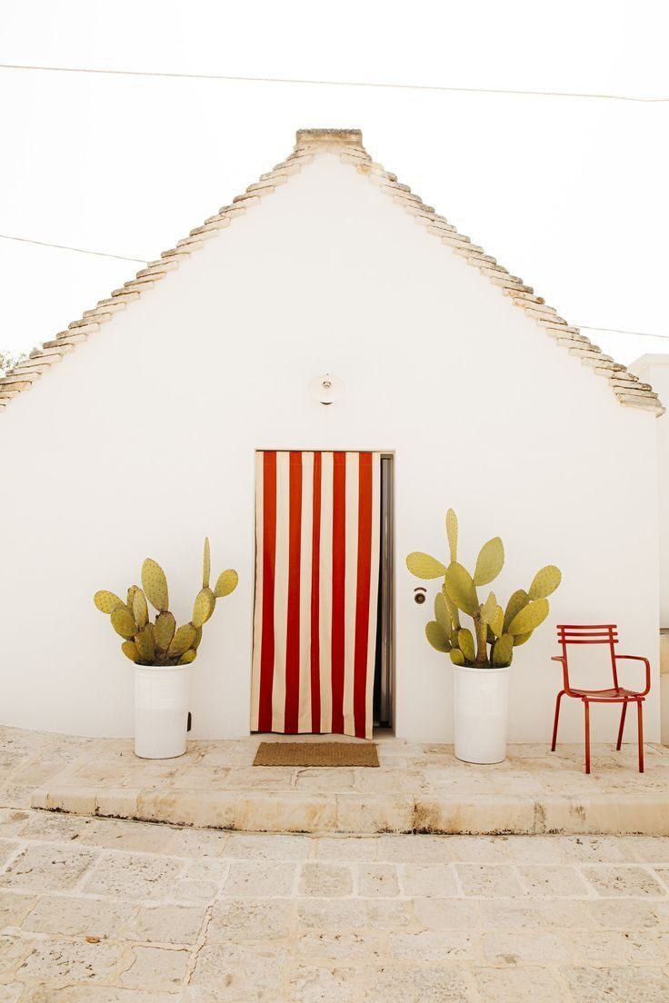 A whitewashed Puglian fa&ccedil;ade with a red and white striped door curtain, prickly pears in white pots either side