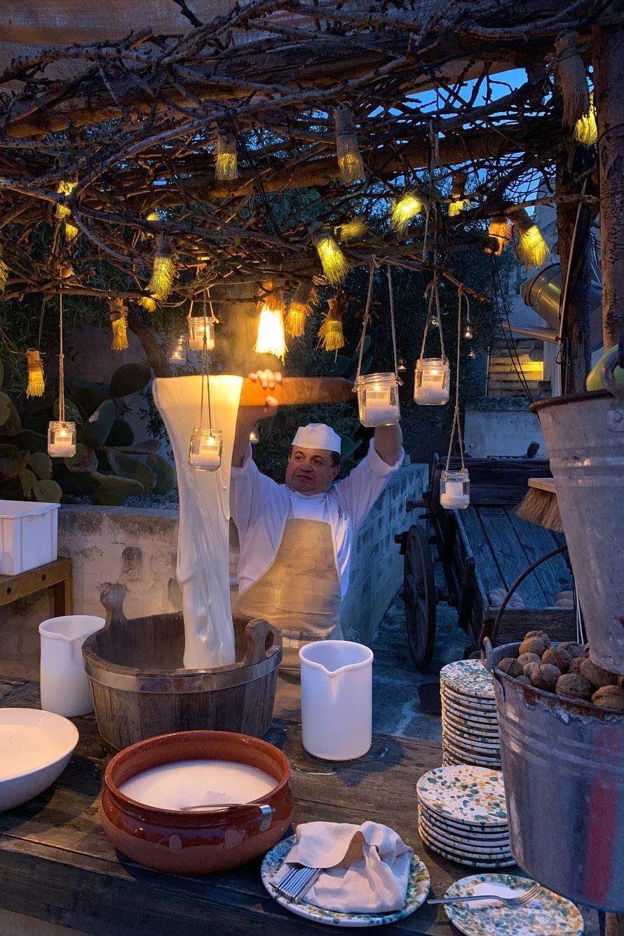 A cheesemaker stretching fresh mozzarella by hand under a pergola hung with lanterns at dusk