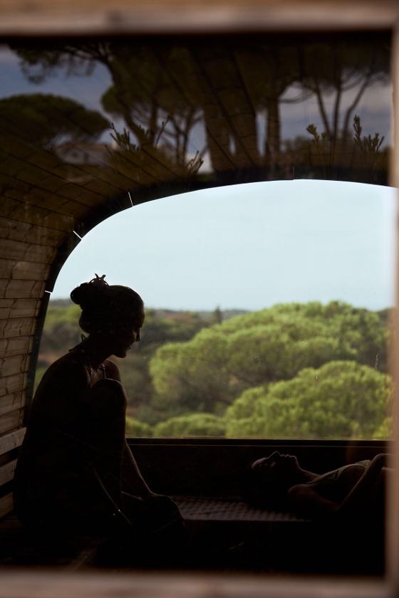A woman in silhouette at an arched window above the pine forest